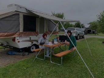 Ground-level photo of an RV/tent/camper site with a pop-up camper, picnic table and adjacent parking — illustrates typical campsite accommodations. Shown on RV/Tent/Camper Sites section.
