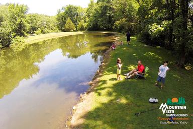 Aerial/overhead view of the campground pond with people along the shoreline — provides an overview of the water feature and adjacent grounds.