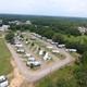 High, clear aerial drone photo showing overall park layout with multiple RV sites, road loop, surrounding trees and nearby development — matches homepage background (DJI_0001) used to show property overview.