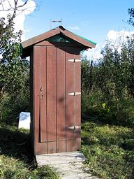 Outhouse at Koknuk Cabin surrounded by vegetation with green plexiglass as roof