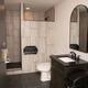 Modern bathroom with black countertop vanity, round mirror, white toilet, tiled shower, and soap dispenser on wall.