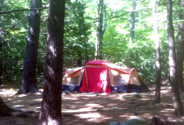 Large tent pitched among trees showing campsite layout and wooded surroundings — useful campsite view from the campground gallery.
