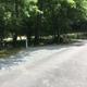 Angled view of campsite and adjacent paved access road with picnic bench and trees — provides additional perspective of site layout and road access shown on the Sites page.