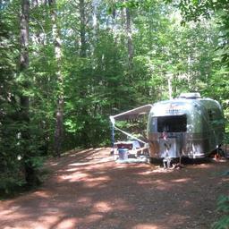 Airstream-style RV parked at a shaded campsite showing an RV pitch, awning and site layout among trees — good example of RV accommodations on site. Source: homepage gallery.
