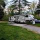 RV parked on a defined gravel/grass site with picnic table and hookups visible — clear example of RV accommodations on the property (photo from site showing actual pitch).