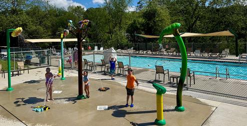 Pool and splash pad with children playing and the adjacent pool visible — clearly shows on-site aquatic recreation facilities (slide image on site highlighting pool/splash area).