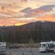 Sunset overview showing multiple RVs parked on gravel pads with mountain backdrop — clear overall view of the RV parking area and surrounding scenery, matching the park layout on the site.