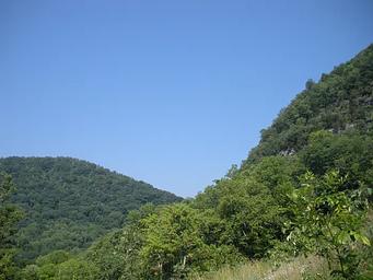 A light blue sky with green mountains.