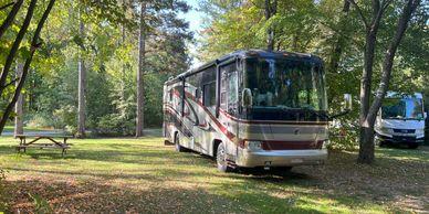 Large RV parked at a campsite with picnic table and trees — shows an on‑site RV pitch with hookups and typical campground layout (from main site gallery).
