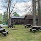 Multiple picnic tables outdoors in grass area on the side of the dining hall facility.  Several large trees shade the picnic area.