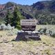 Yellow and brown campsite sign mounted on a rock pedestal. Trees, mountains and a little bit of blue sky are in the background.