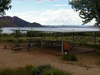Pavillion over picnic tables in a group area. There is a firepit with benches and two grills off to the side. 