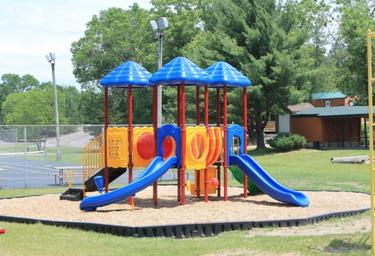 Colorful children’s playground equipment (slides, rubber mulch area) located on manicured lawn — illustrates family-friendly playground amenity on the property listing.