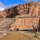 A dirt road cuts through a wide canyon of orange cliffs with a bathroom in the distance.