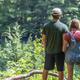 Over-the-shoulder view of two visitors looking down at the pond and wooded shoreline — clearly shows the on-site natural scenery and trails context (page: Explore / homepage hero).