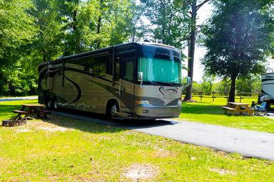 Active RV parked on a paved site with picnic table and grassy area — shows RV pitch layout and level of vehicle accommodation (source: site homepage).