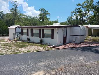 Exterior view of a manufactured home/unit on a paved site with surrounding trees — shows the type of onsite units and lot layout (from the 'Units For Rent/Sale' page).