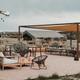 Wide view of an outdoor seating/communal area with shade structure, tables and lounge seating — useful for showing on-site guest facilities and gathering space (photo is on the property website).