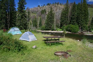 Two tents pitched at a campsite with a firepit and picnic table along  Slough creek