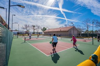 Active recreational area showing pickleball/tennis courts with residents playing and surrounding buildings — demonstrates on-site amenities and community activity (matches site’s community images).