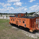 Ground-level view of the orange caboose feature with the clubhouse and RV sites visible in the background — distinctive property landmark that reinforces the resort’s name and theme (source: Home page).