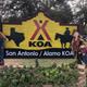 Clear on-site entrance sign for 'San Antonio / Alamo KOA' with landscaping and campground buildings visible behind — a strong property-identifying photo from the campground's main page.