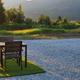 Sunlit campsite vignette with table, chairs and a fire ring on gravel pad looking toward the lake/landscape — shows guest seating/amenity detail used in the property's listing.