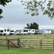 Ground-level view of multiple parked RVs behind a gate and pasture — good for demonstrating campsite density and rural setting (from About Us page).