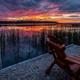 Sunset lakeside view with Adirondack chair on a small shore area — highlights waterfront guest seating and scenic views from the property (homepage gallery image).