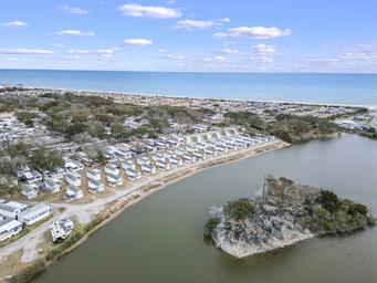 Aerial view highlighting cabins or mobile units beside an inland pond and the beach — good for showing campsite variety and on-site water features (source page: hurricane FAQs).