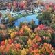 High-resolution aerial view showing the campground layout: pond, surrounding RV/cabin pads, walkways and trees in fall colors. Matches the site hero image and page context for Erie KOA Holiday.
