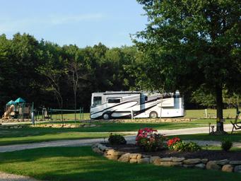 Large RV in a landscaped area with playground nearby — shows open RV sites, landscaping and family-friendly facilities (Rates/Reservations page).