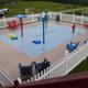 Overhead view of fenced splash pad/water play area with surrounding chairs and campground in background — shows an amenity on the property (Events / amenities context). 