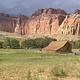 A old barn sites in a grass field. A red rock cliff is the background.