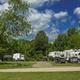 Wide daytime view of the campground showing multiple RVs parked along a road and open grassy areas — good overall site/roadway overview (image used as a slideshow background on the property site).