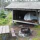 Tent shelter, fire ring and picnic table on grassy hillside.