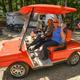 Guests in a decorated golf cart with RVs and wooded campsites in the background — highlights guest experience and campground roadways/parking areas (from site gallery).