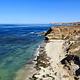Sandy beach with ocean, small waves and steep coastal bluffs covered in dry grass.