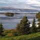 A glassy lake reflects mountains, low clouds, and spruce trees.