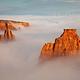 Independence Monument, a tall red rock pillar, rises above a blanket of clouds