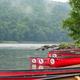 Row of red canoes pulled up on the shore beside the river — depicts equipment and riverfront launch area used by the property (campground page).