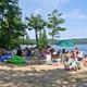 Beach scene with campers, chairs and lake in background — illustrates the campground's sandy swimming area and family recreation on Long Lake.
