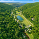 High-resolution aerial view of the entire campground valley showing the pond, pool area, roads and RV/cabin rows — strongly matches the site’s aerial/virtual tour imagery on the property website.