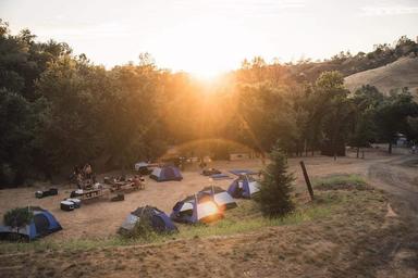 Sunset view of a tent camping area with multiple tents and communal fire/picnic area — illustrates tent camping and the campground’s scenic setting at dusk.