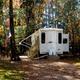 Photo of a single RV/park model set in a wooded campsite with an American flag — suitable campsite view from the site's 'Seasonal' and 'Gallery' context.