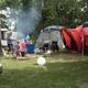 Active tent campsite scene with tents, chairs and a vehicle in a wooded site — useful depiction of tent camping options; originates from the site's campsites imagery.