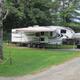 Clear photo of an RV parked on a gravel/pad site with hookups visible and campground road — shows typical RV accommodations on the Littleton / Franconia Notch KOA property (from the site's 'ways to stay' images).