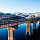U.S. Highway 50 crosses Blue Mesa Reservoir on Middle Bridge, with snow capped hills in the background.