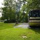 Wide shot of an RV parked on a gravel/grass site with hookups visible — good example of RV accommodations and site layout (page: Accommodations).
