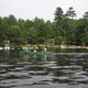 Clear waterfront view showing canoes/kayaks on the lake with the campground shoreline and buildings visible behind the treeline — strong depiction of on‑site water recreation and lakeside setting from the site's Photos section.